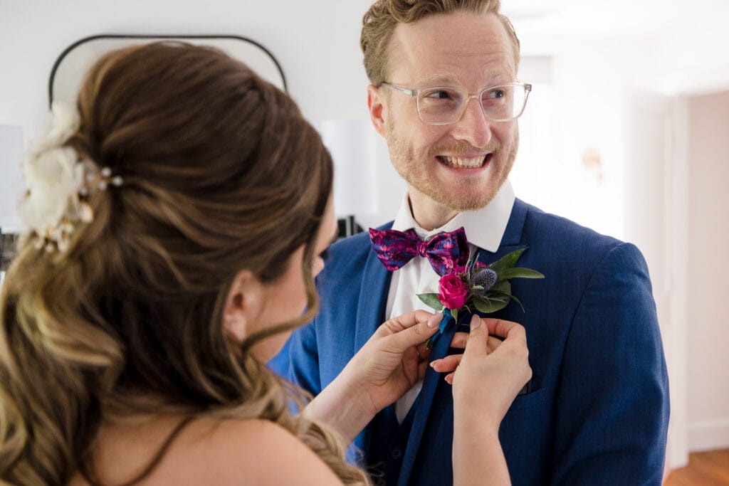 A groom smiles as the bride adjusts his boutonnière