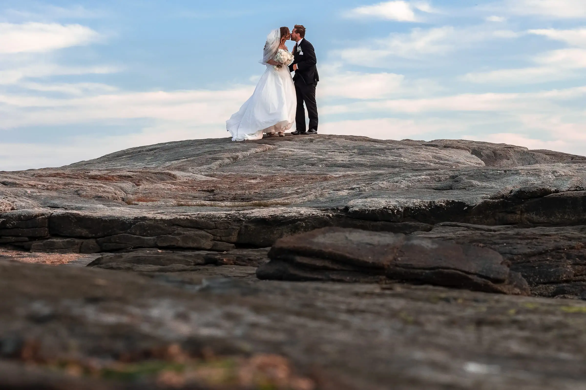 A bride and groom kissing atop a large rock