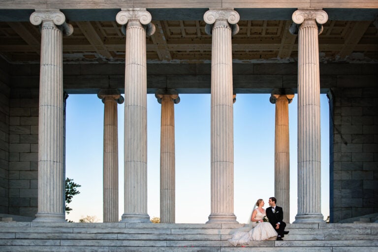 A bride and groom sitting next to each other on the steps to the temple of music in providence