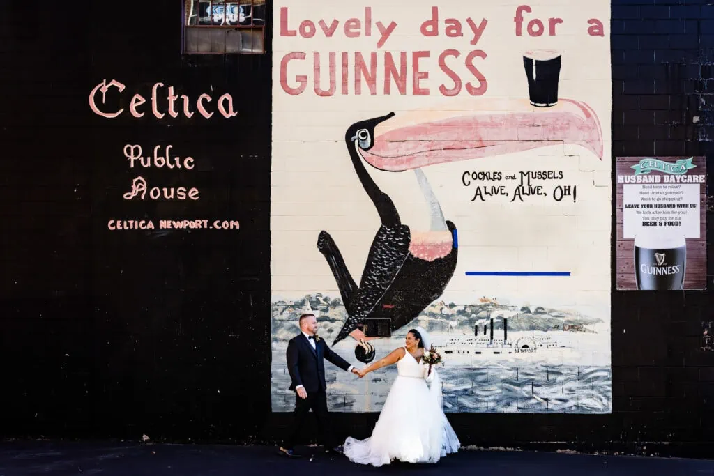 A woman dragging a man across a parking lot with a guinness mural painted on a wall behind them