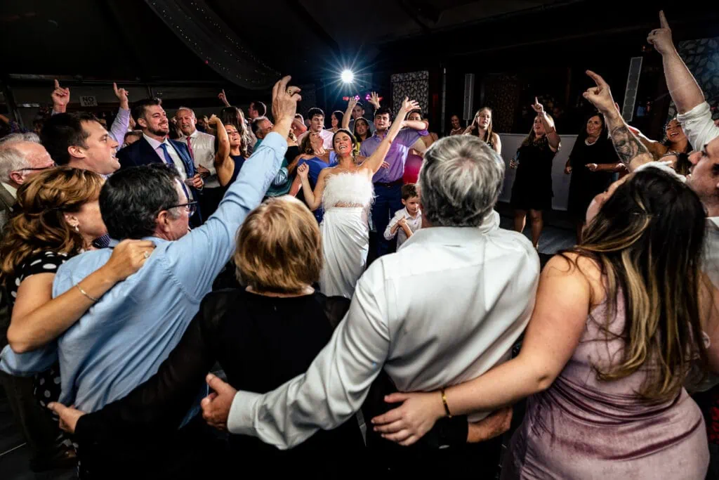 A crowd of people circle a bride with her hand up in the air at a Castle Hill Inn wedding