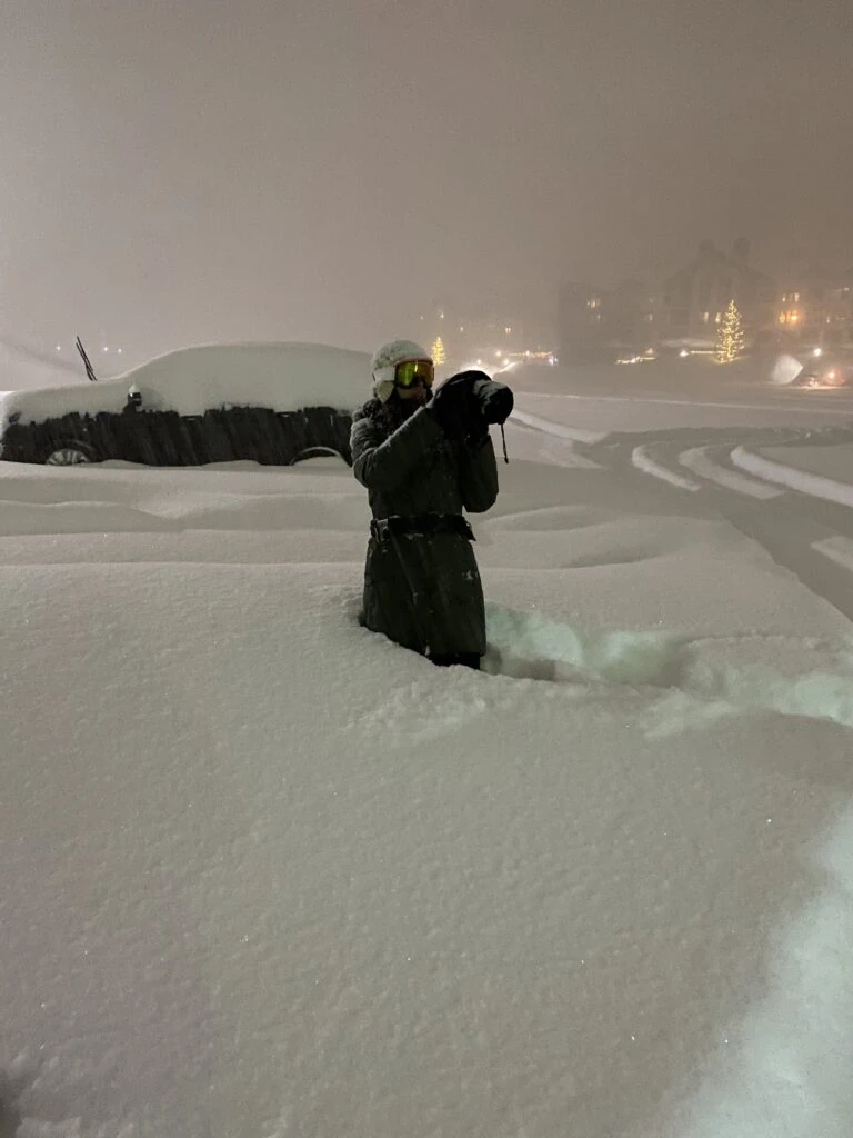 A woman holding a camera standing in waist deep snow at night
