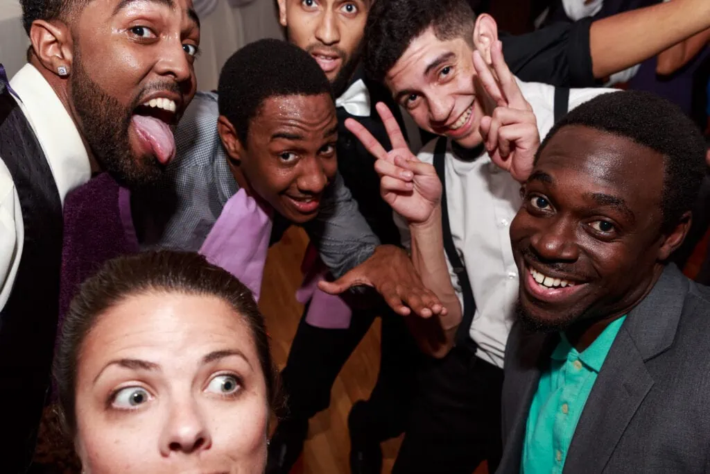 A selfie of a woman with several men throwing peace signs and sticking out their tongues