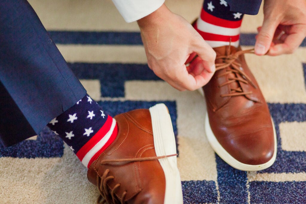 Hands adjusting the ties on brown leather shoes with american flag printed socks