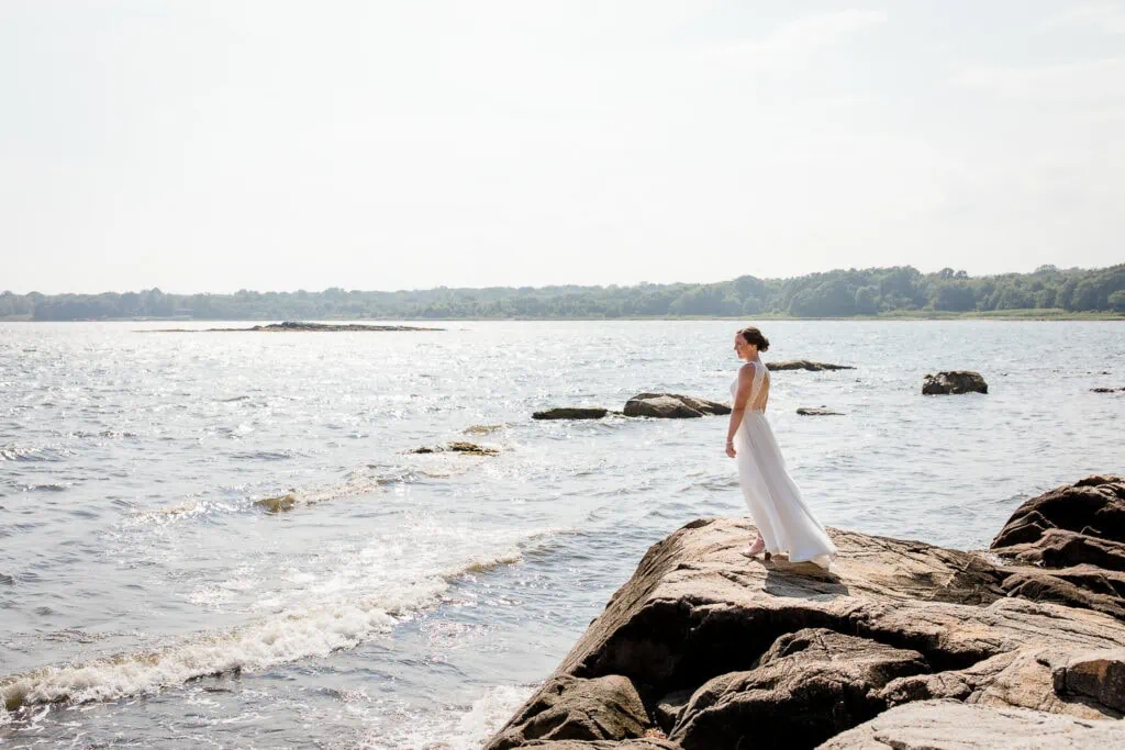 A bride stands on a rocky outcropping by the edge of the ocean