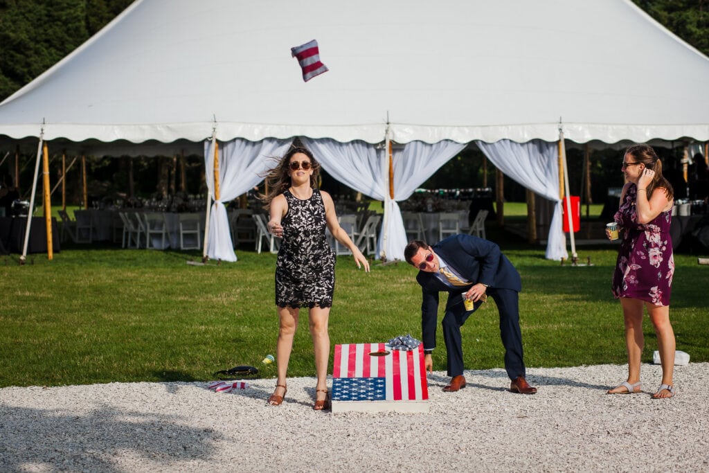 A woman throws a red and white beanbag from an american flag patterned cornhole set
