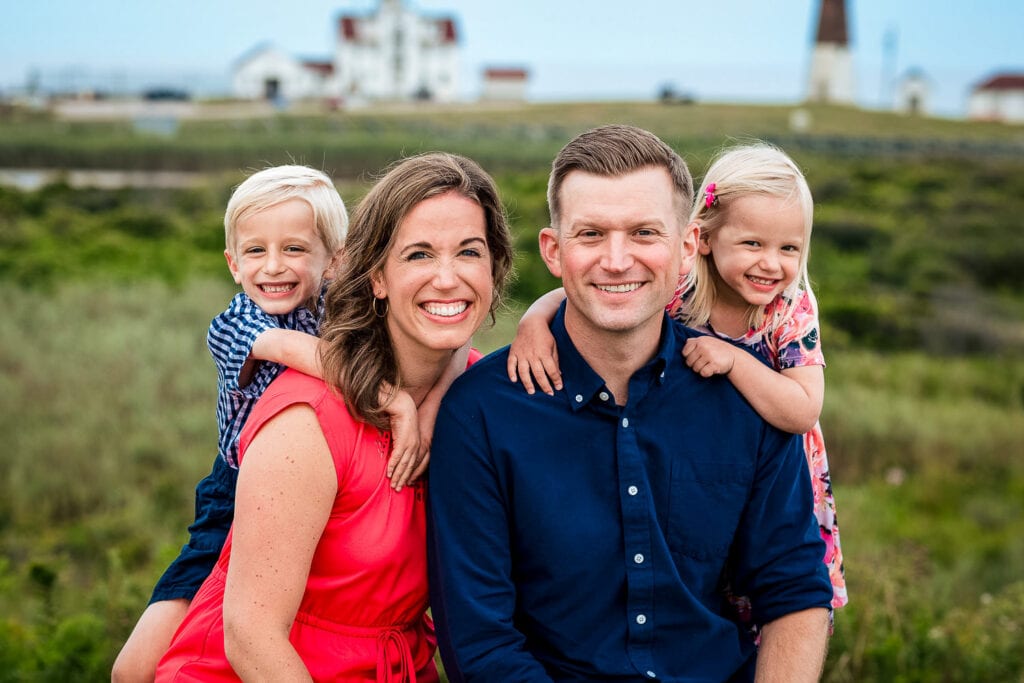 A family of four poses by the Pt Judith Lighthouse for family photos