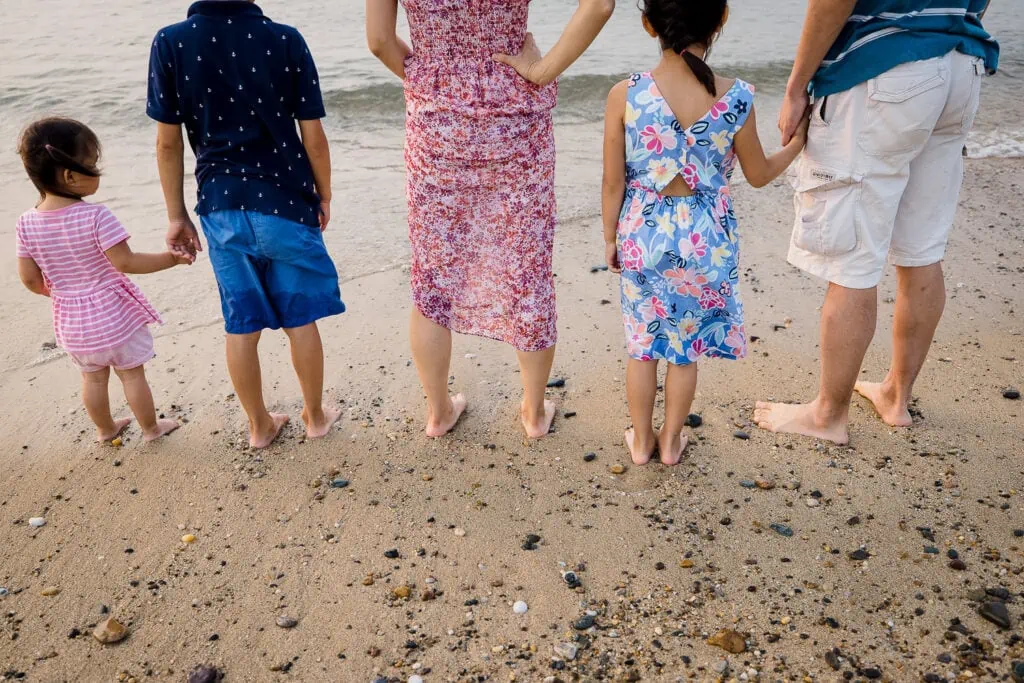 A family of 5 hold hands and look out at the ocean