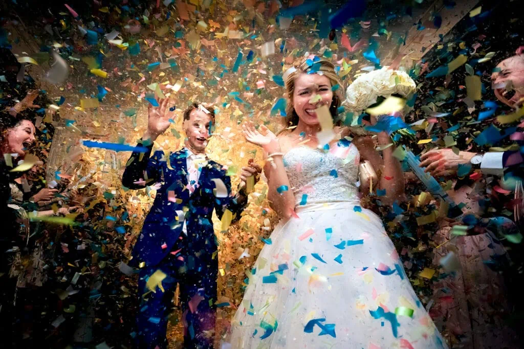 A bride and groom smile and run through a ton of confetti