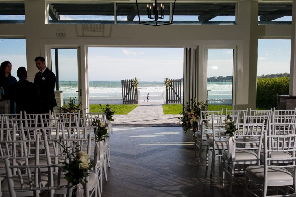 A view of chairs inside looking through a glass accordion door to the outside lawn and beach
