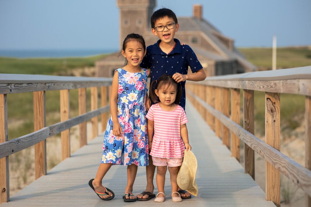 Three children wearing navy and pink stand on a boardwalk