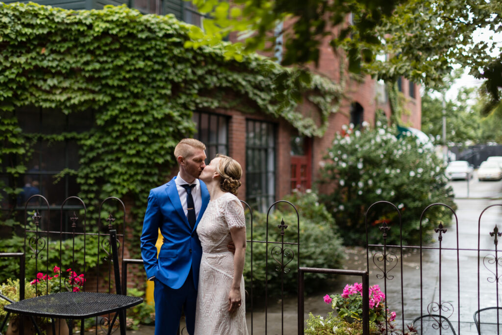 A bride and groom kiss in a brick courtyard with lots of ivy