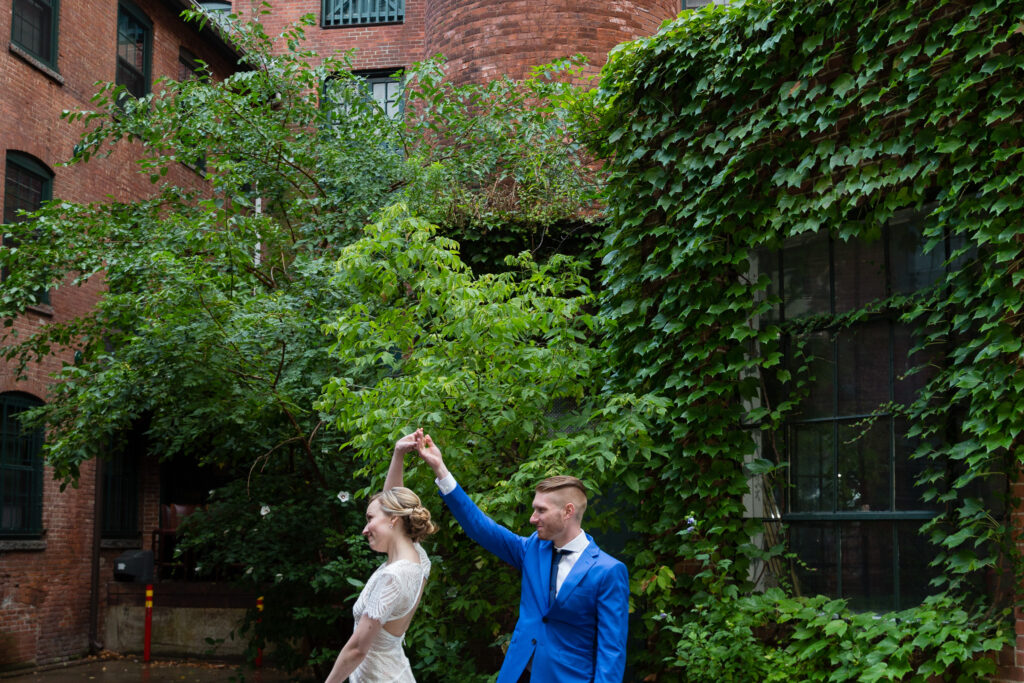 A bride and groom dancing in a brick industrial courtyard with ivy covered walls