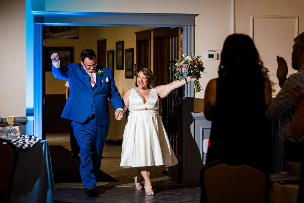 A bride and groom smile and throw their hands in the air as they enter the room