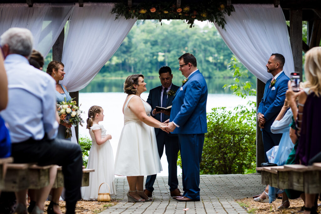 A bride and groom holding hands by a lake