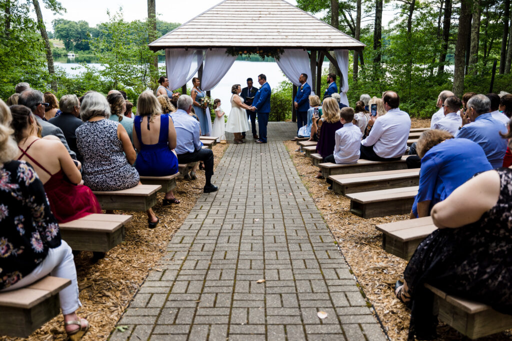 A bride and groom holding hands at their wedding ceremony at an outdoor pavilion by a lake