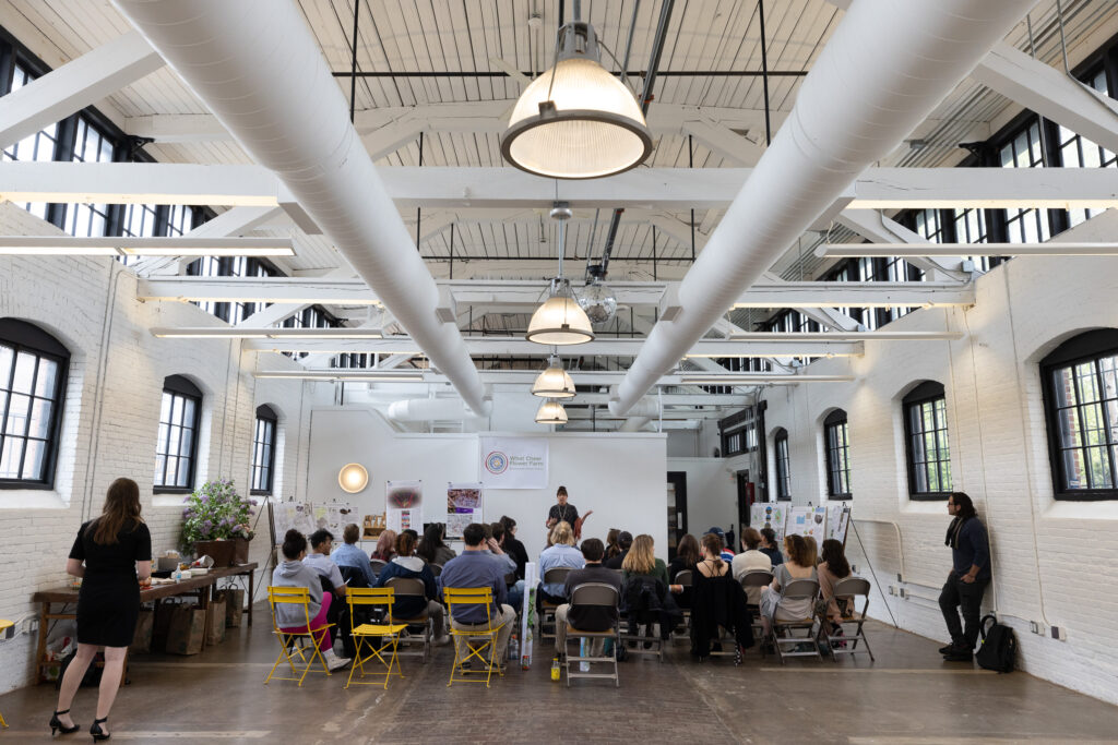 A group of people watching a presentation in a white industrial space that is a rhode island wedding venue called the dye house