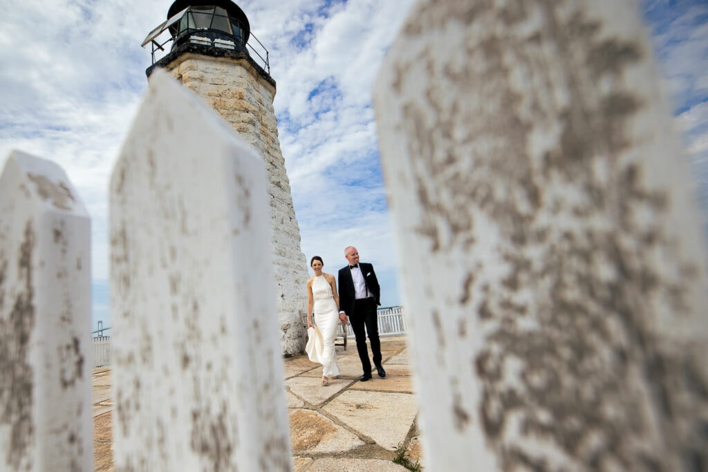 A bride and groom walking by the newport harbor lighthouse