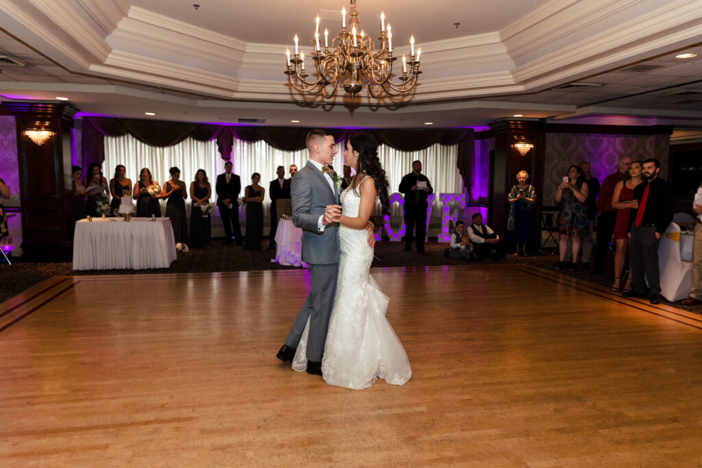 A bride and groom sharing their first dance under a chandelier in a ballroom