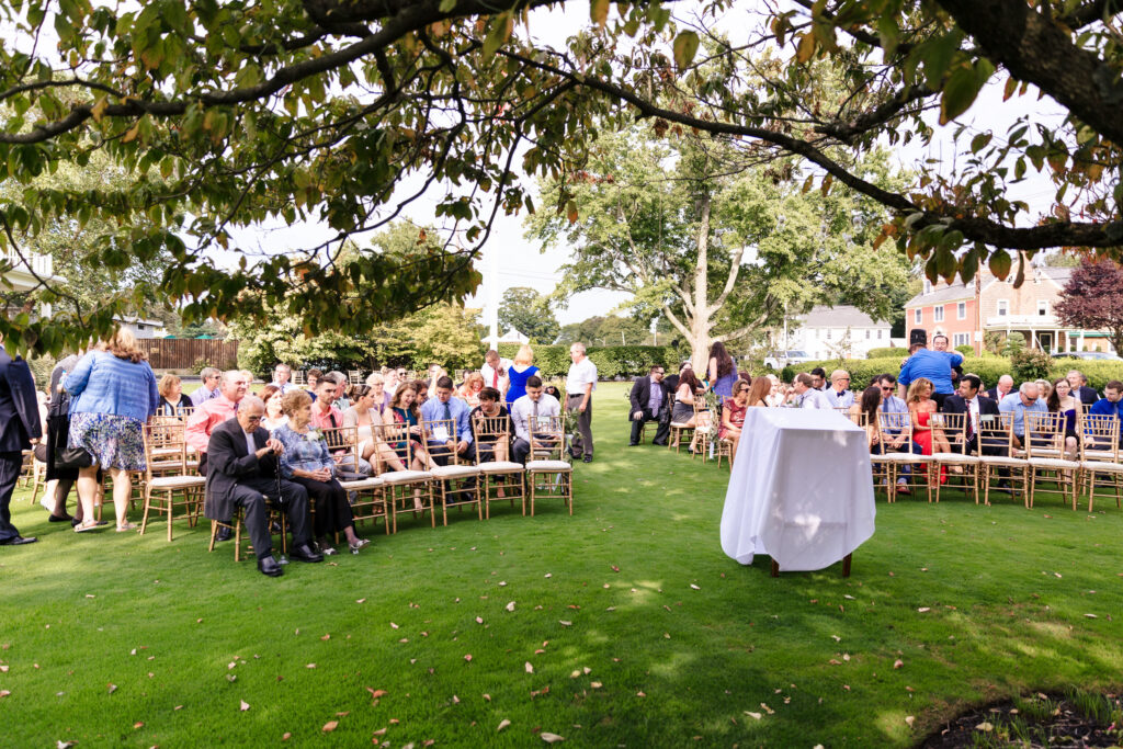A wedding ceremony with guests seated in a garden under a tree