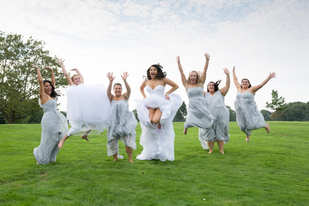 A bride and bridesmaids jumping in the air on a golf course