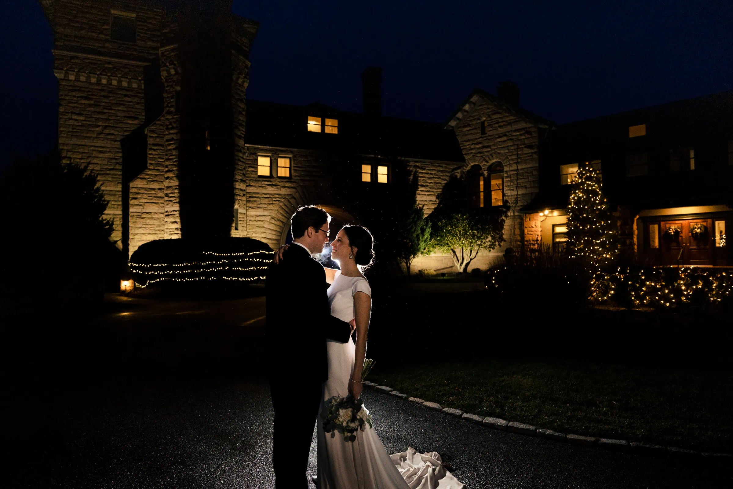 A bride and groom backlit against a mansion at night at their winter wedding in newport